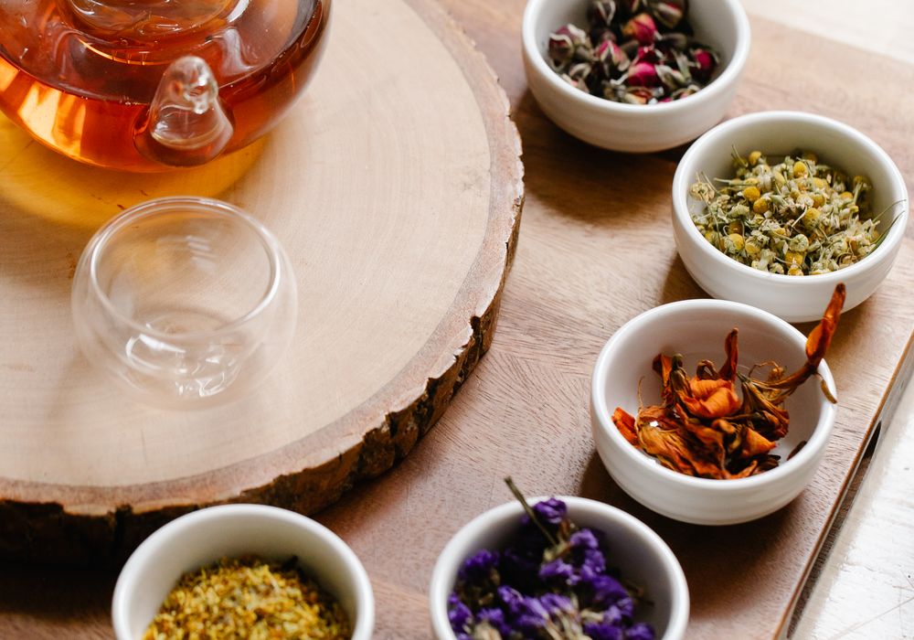 Bols de plantes médicinales séchées et théière en verre posés sur un plateau de bois clair